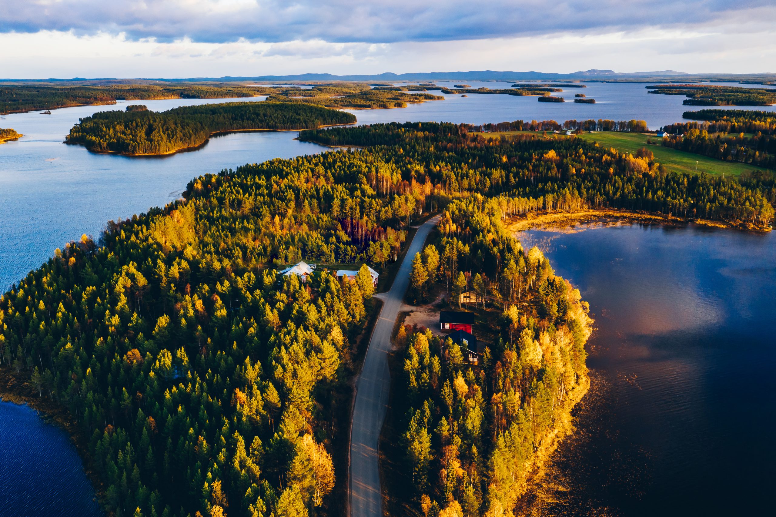 Aerial view of road through autumn forest with blue lakes in Finland.