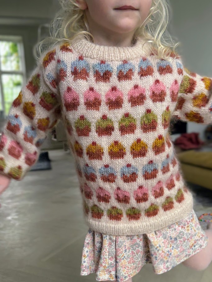 Dansende pige i farvestrålende strikket sweater med små kager på