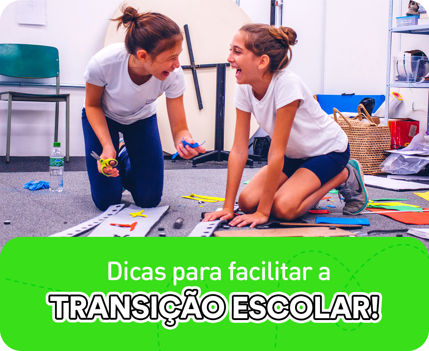 Duas crianças em fase de transição escolar no ambiente de aprendizagem, sorrindo e conversando ajoelhadas, enquanto estão com a mão na massa produzindo um trabalho manual.