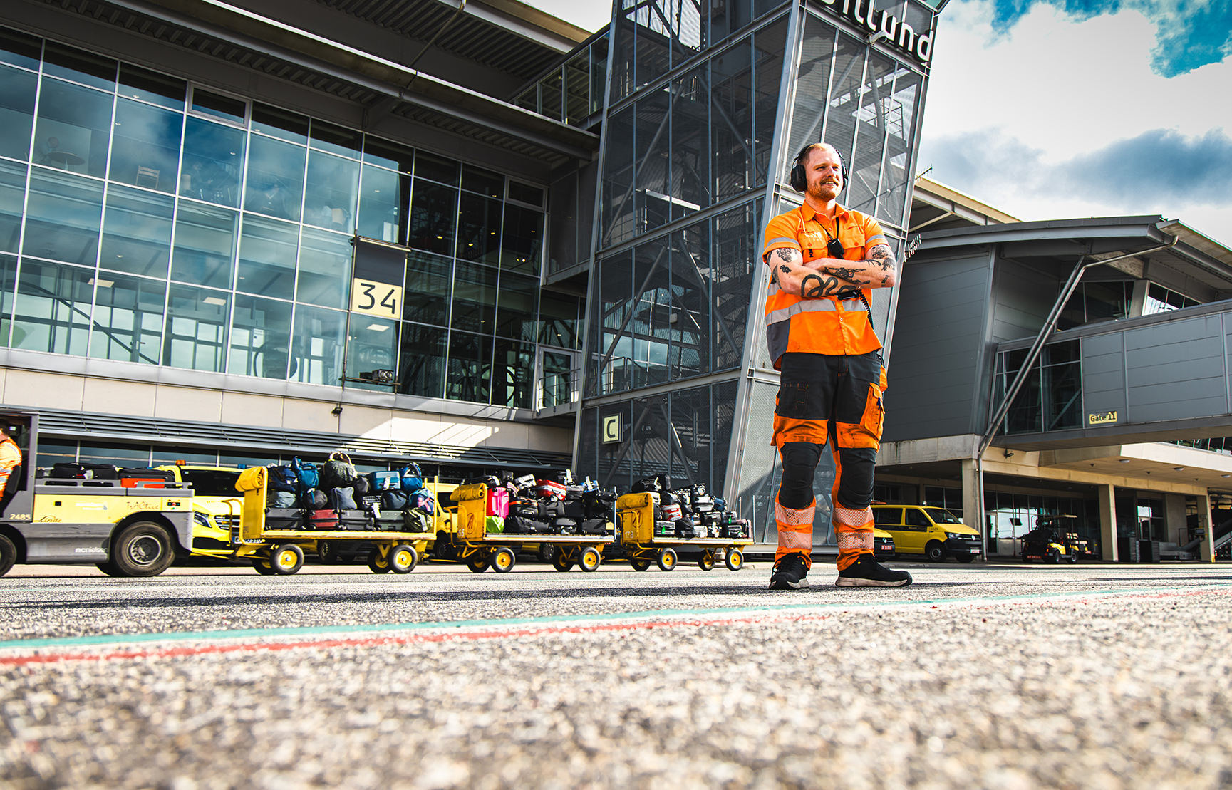 Ground worker i Billund Lufthavn – portrætfoto i arbejdsmiljø på rampen med bagagevogn i bevægelse.