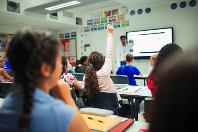 A photo of a child raising their hand in a classroom as children prepare to back to school and parents want to know when the next school holiday after summer is