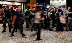 Riot police wait at a Mass Transit Railway (MTR) station as commuters walk past in Hong Kong