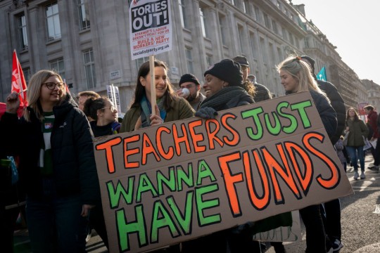 Teachers Strike In London with a group of women holding a placard that says 'Tories Out!' and a large cardboard sign, painted in orange and green: 'Teachers just wanna have funds'.