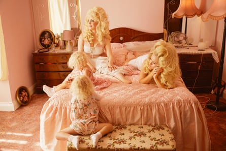 Dolly Parton lookalikes Alice Hawkins and Trixie Malicious, lying on a bed with a pink cover on it, London, 2019