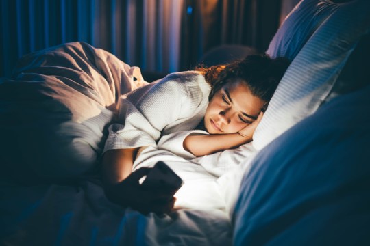 Young woman laying in bed awake on her phone