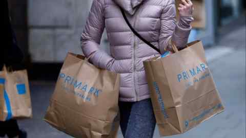 A woman carries multiple Primark shopping bags while walking on Oxford Street in London