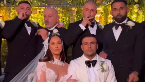 Vicky Pattison/Instagram Pattison, in a wedding gown, and Ramadan, in a white suit, look at the camera with their groomsmen in the background smoking cigars