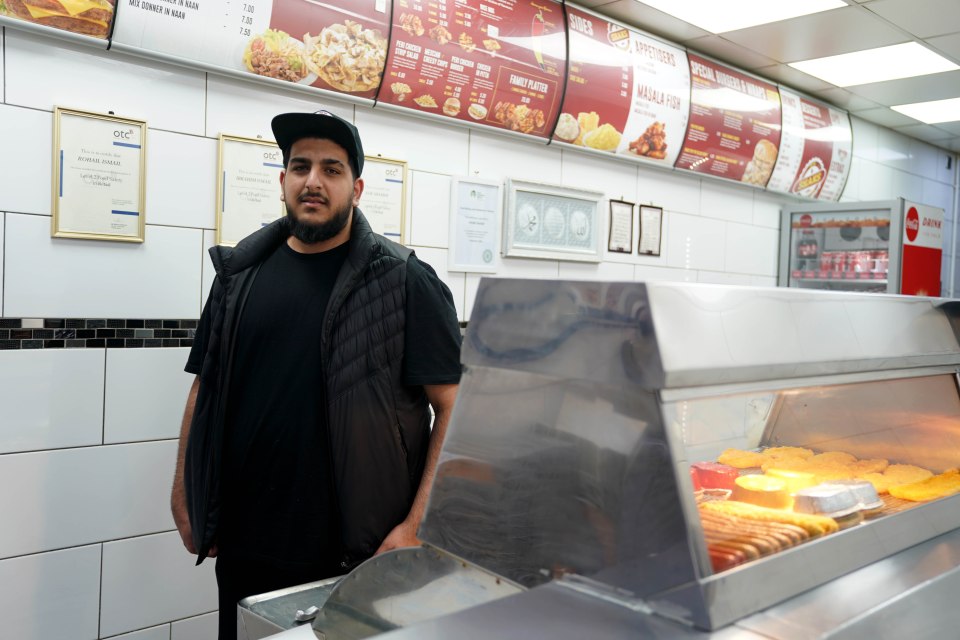 A fish and chips shop worker stands in front of a display case.