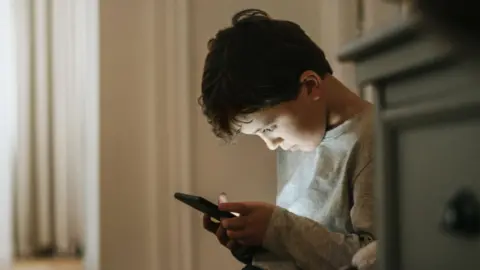 Getty Images A young boy stares down at a smartphone.