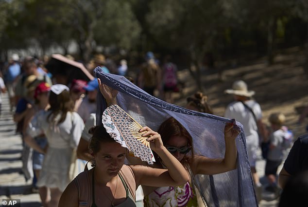 Tourists take cover from the sun outside the entrance of the Acropolis hill during a heat wave in Athens, Wednesday, July 9, 2025