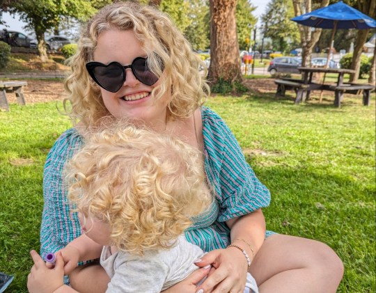 Rose Stokes sitting on the grass outside in a sunny park with her son