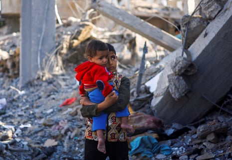 A Palestinian boy carrying a baby stands at a site of an Israeli strike in Rafah in the southern Gaza Strip, amid the conflict between Israel and Hamas, 4 December