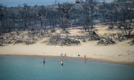 A woman enters the sea from a beach where wildfires destroyed the woods, at Glystra near the village of Gennadi in the southern part of the Greek island of Rhodes, 27 July