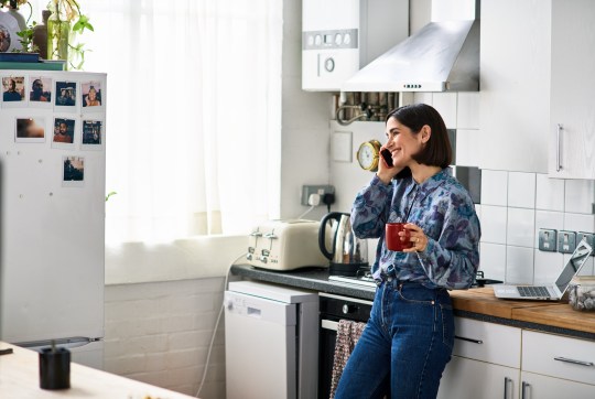 Cheerful woman on phone in kitchen drinking coffee