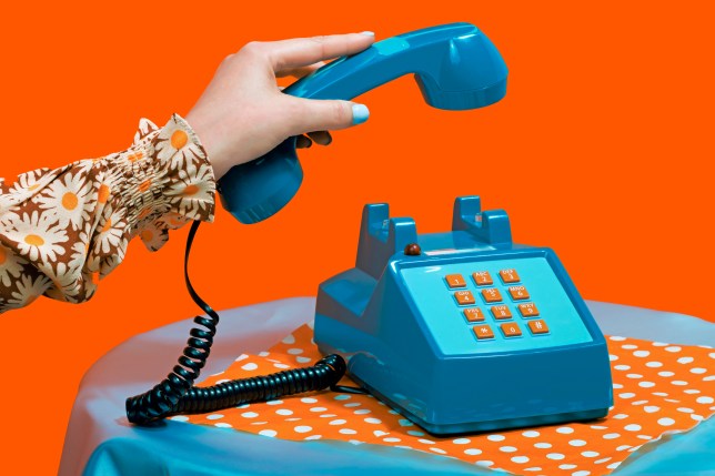 Hand of woman picking up telephone receiver against orange background