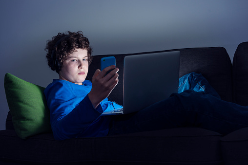 child watching his phone and laptop in a dark room