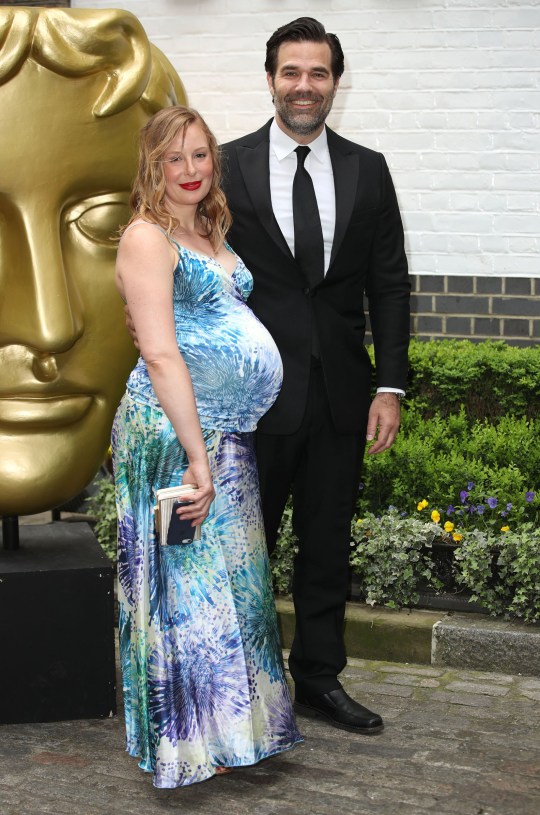 Actor Rob Delaney and his pregnant wife, Leah, pose in front of a giant gold head for photos