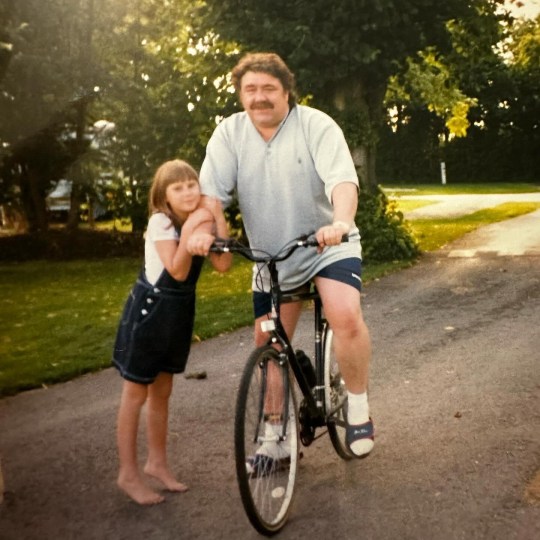 Sophie Hinchliffe as a child with her dad who is riding a bike