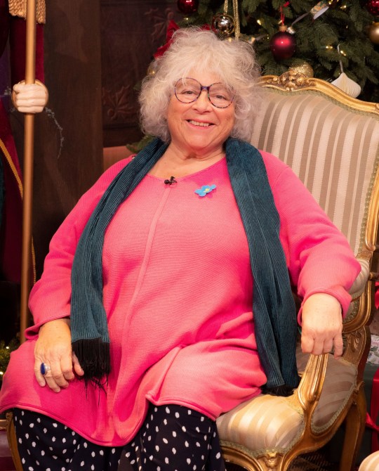 Miriam Margolyes wearing a pink jumper, spotted skirt, and blue scarf while smiling during an appearance on This Morning