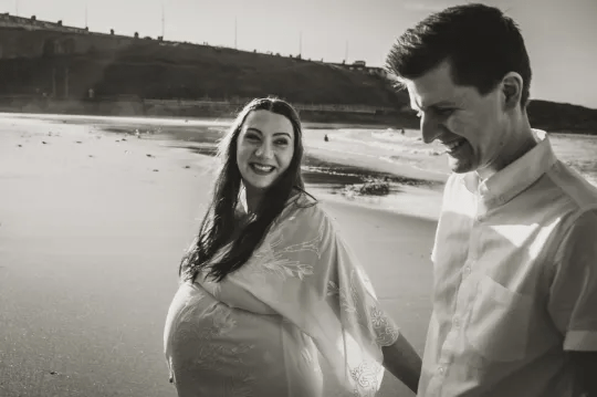 A black and white photo of Ruth and her husband at the beach, holding hands and walking