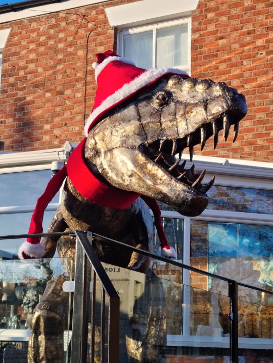 PIC FROM Kennedy News/Miola (PICTURED: THE T-REX SCULPTURE AT MIOLA IN HOLMES CHAPEL, CHESHIRE, AT CHRISTMAS) A dad gave his dinosaur-mad son a 21st birthday present he'd never forget - a 7ft tall T-REX statue that 'roars' at his neighbours from the driveway. Matthew Riddell-Rovira saw homeware shop Miola, in Holmes Chapel, Cheshire, was closing down and selling its iconic metal dinosaur sculpture. When he asked dad Dave Rovira to buy it the 56-year-old was going to reject the 'wild' idea but mum Blanch Rovira thought it'd make a great early 21st birthday present. DISCLAIMER: While Kennedy News and Media uses its best endeavours to establish the copyright and authenticity of all pictures supplied, it accepts no liability for any damage, loss or legal action caused by the use of images supplied and the publication of images is solely at your discretion. SEE KENNEDY NEWS COPY - 0161 697 4266