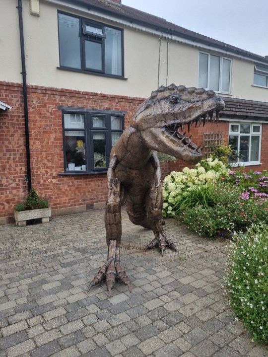 PIC FROM Kennedy News/Miola (PICTURED: THE GIANT T-REX SCULPTURE ON THE FAMILY'S DRIVEWAY) A dad gave his dinosaur-mad son a 21st birthday present he'd never forget - a 7ft tall T-REX statue that 'roars' at his neighbours from the driveway. Matthew Riddell-Rovira saw homeware shop Miola, in Holmes Chapel, Cheshire, was closing down and selling its iconic metal dinosaur sculpture. When he asked dad Dave Rovira to buy it the 56-year-old was going to reject the 'wild' idea but mum Blanch Rovira thought it'd make a great early 21st birthday present. DISCLAIMER: While Kennedy News and Media uses its best endeavours to establish the copyright and authenticity of all pictures supplied, it accepts no liability for any damage, loss or legal action caused by the use of images supplied and the publication of images is solely at your discretion. SEE KENNEDY NEWS COPY - 0161 697 4266