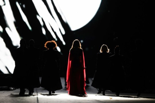 Taylor Swift, flanked by backup singers, silhouetted as she walks on stage for folklore and evermore eras during Eras Tour 