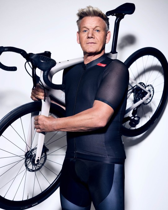 Gordon Ramsay holds a bike as he looks at the camera