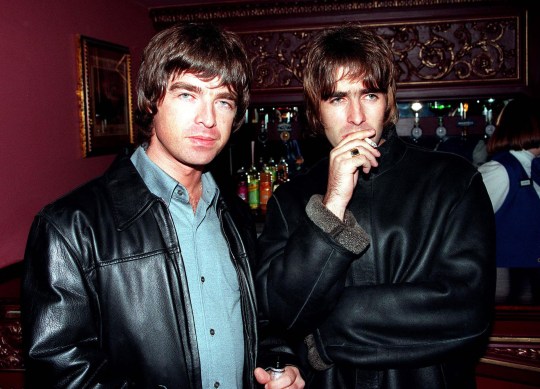 Oasis' Liam Gallagher and Noel Gallagher stand together in pub in 2000s. Liam (R) holds cigarette to mouth while Noel looks at camera. Both wear leather jackets.