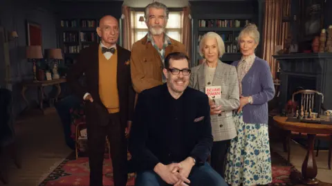 Netflix Richard Osman on the set of The Thursday Murder Club with cast Sir Ben Kingsley,  Pierce Brosnan, Dame Helen Mirren and Celia Imrie in costume