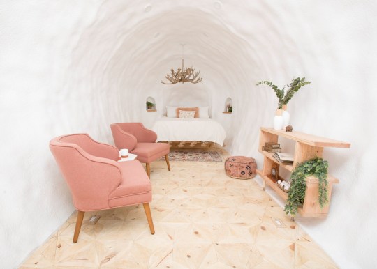 Inside the white interior of the Big Idaho Potato Hotel, which has a shelf, two pink chairs, and a white bed