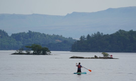 A paddleboarder in the water of Loch Lomond, in the village of Luss in Argyll and Bute, Scotland. Temperatures have reached 40C for the first time on record in the UK, with 40.2C provisionally recorded at London Heathrow, the Met Office has said. Picture date: Tuesday July 19, 2022. PA Photo. See PA story WEATHER Heatwave. Photo credit should read: Andrew Milligan/PA Wire