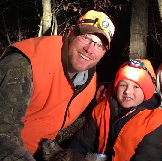 Ryan Beierman (L) and his son Owen Beierman (R) wear matching orange outfits and headlights as they pose in the woods in the dark