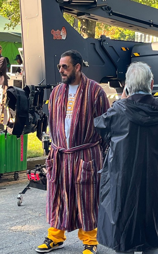 Adam Sandler on the set of Happy Gilmore 2. He is wearing a red striped bathrobe and black sunglasses