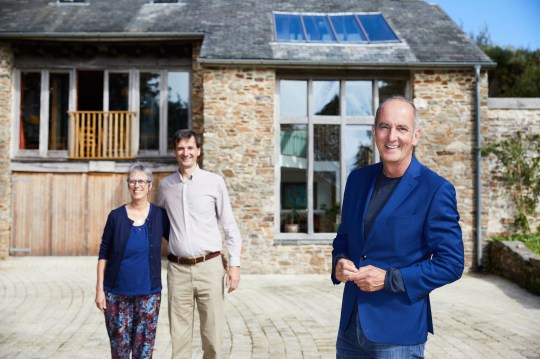 Kevin McCloud standing in front of transformed derelict barns with owners Sue and Martin on Grand Designs