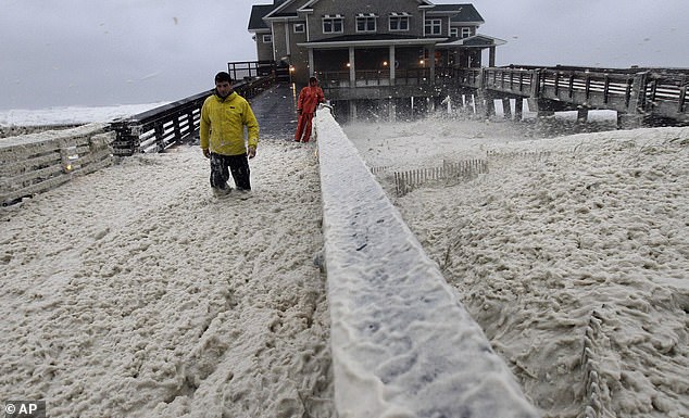 A news crew (pictured) wades through sea foam blown onto Jeanette's Pier in Nags Head, North Carolina on October 28, 2012 - when wind and rain from Hurricane Sandy hit the area