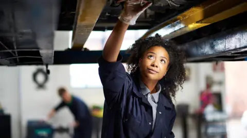 Getty Images Female mechanic working on the underside of a car