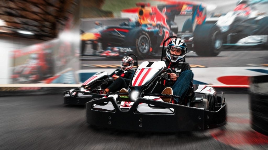 Image of person driving kart at K1 Speed venue. An F1 car on the wall is in the background