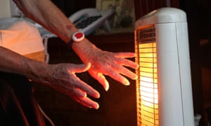 An older lady holds her hands close to an electric fire