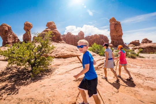 A happy family hiking together in the beautiful rock formations of Arches National Park. Walking along a scenic trail with large rock unique formations in the background