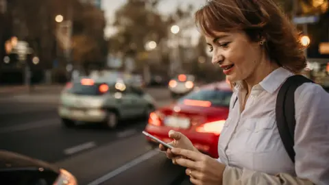 Getty Images Woman by a busy road looking at her phone waiting for a ride