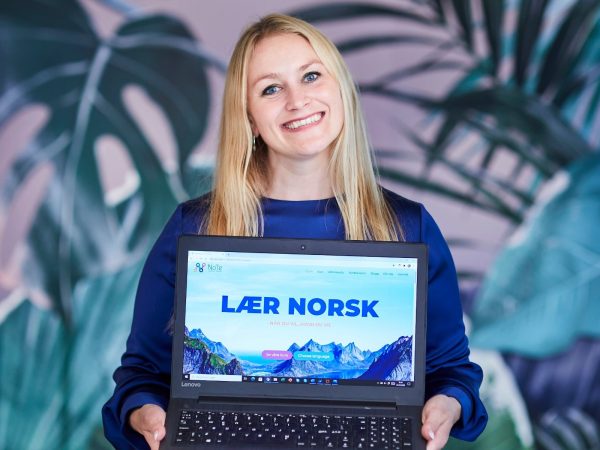 Karense Foslien holder en laptopp hvor det står "Lær norsk".