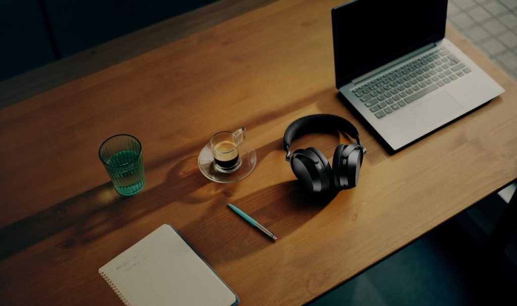 Sennheiser Momentum 5 hörlurar på ett skrivbord med en laptop och en kaffe samt ett anteckningshäfte.