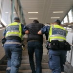 två ordningsvakter leder en man mellan sig uppför en trappa
