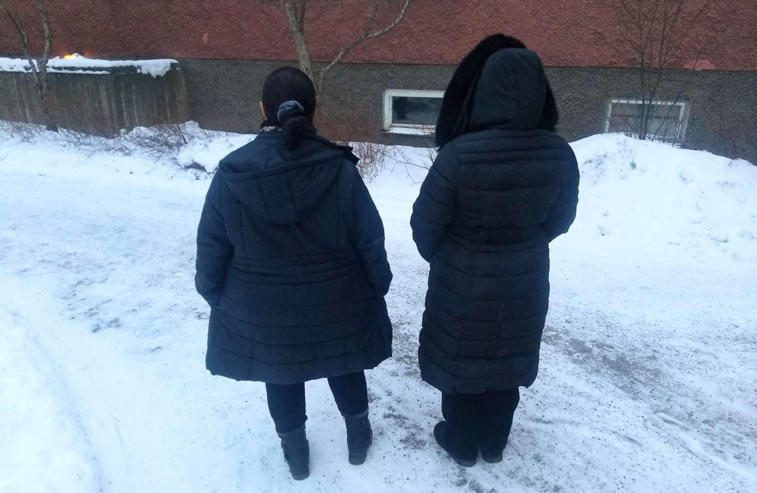 två kvinnor i ytterkläder står med ryggen mot kameran