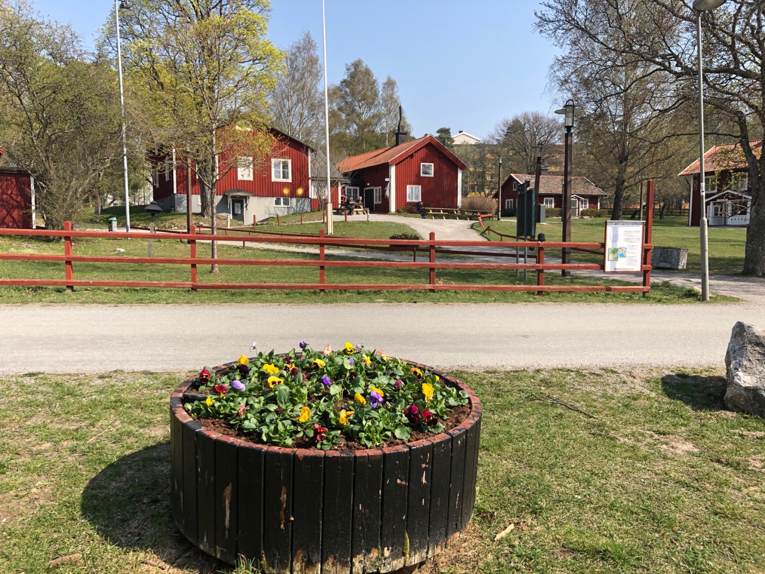 Blomrabatt i förgrund. Husby gård i bakgrunden, solig sommardag.