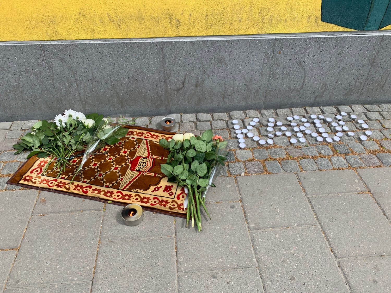 minnesplats efter den mördade i Husby. Blommor, en matta och värmeljus.
