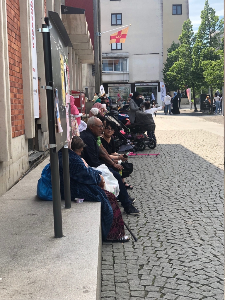 Folk sitter i skuggan vid torget.