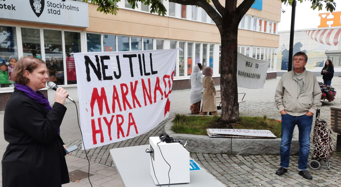 Kvinna med mikrofon och banderoll mot marknadshyra