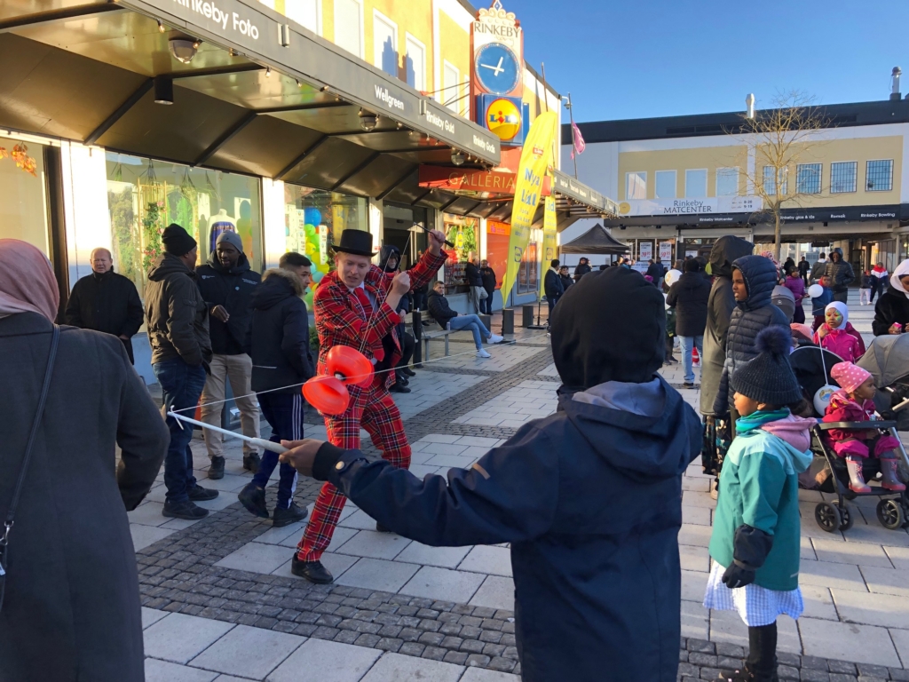 en man i rödrutig kostym jonglerar på rinkeby torg